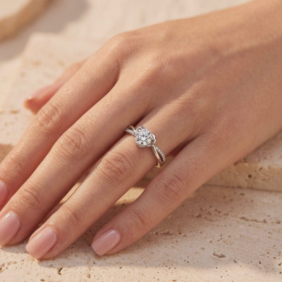 Silver heart-bypass ring with a round center gem and pave accents, worn on a hand.
