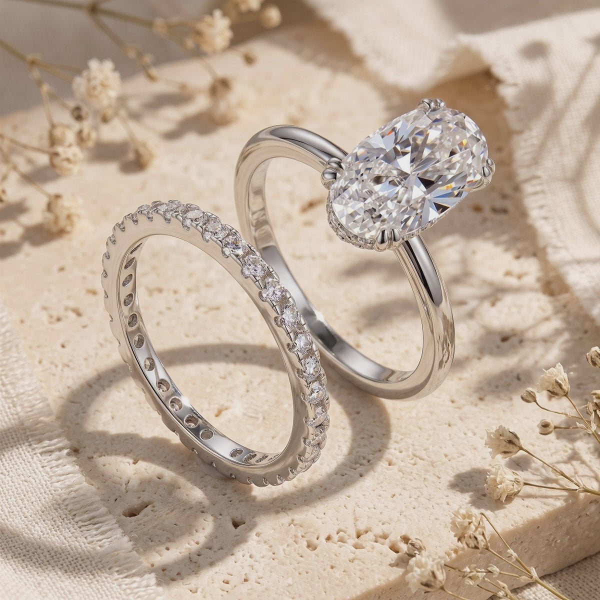 Silver oval solitaire ring and pavé eternity band displayed upright on a textured stone surface.