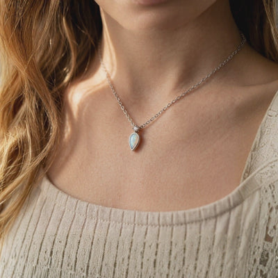 Teardrop opal pendant necklace with a clear accent stone worn around a model's neck.