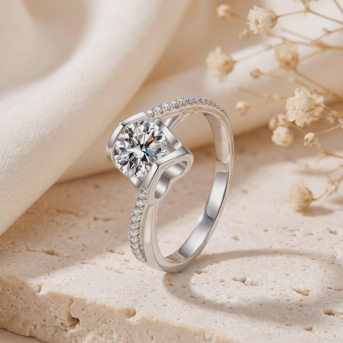 Angled studio view of a silver ring with a round clear center stone, heart motif beneath the setting, and pavé bypass shank.