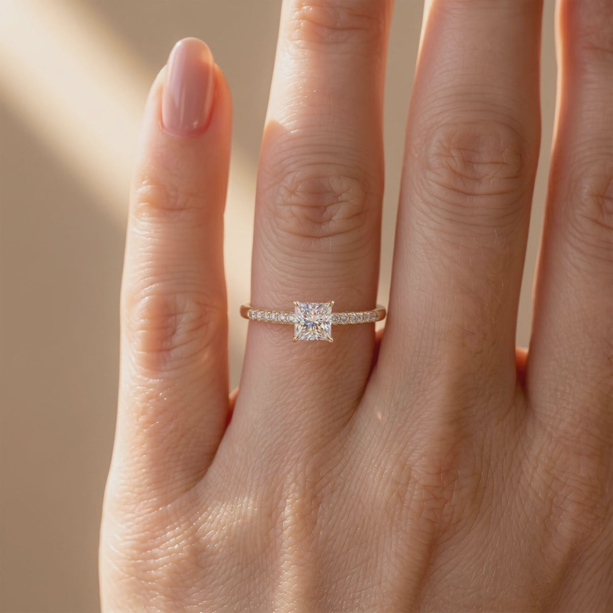 Yellow gold-tone pavé solitaire ring with a square princess-cut center stone, shown worn on a finger.