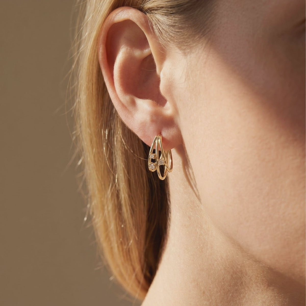 Close-up profile of a model wearing one gold multi-row hoop earring with round moissanite stones.