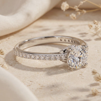 Close-up of the silver Josephine ring with a round clear stone and pavé band resting on a beige surface.