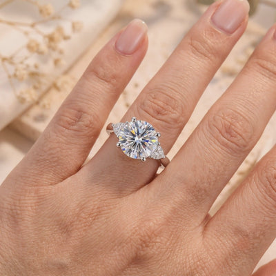 Silver trilogy ring with a large round center stone and pear-shaped side accents worn on a finger.