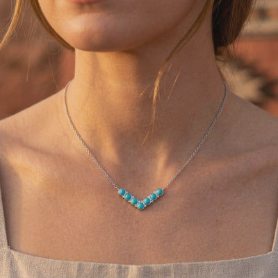 Silver necklace with a V-shaped row of turquoise stones, shown worn at the collarbone.