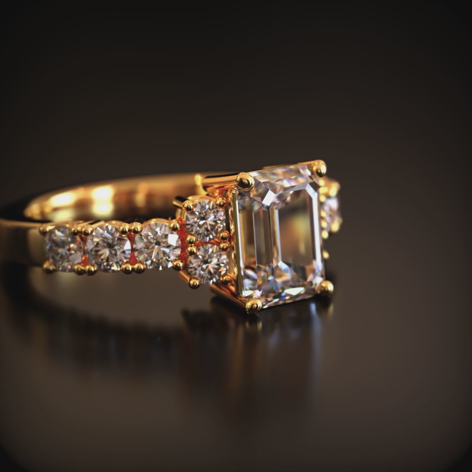 A solid gold ring with an emerald-cut center stone and small round side stones on a dark reflective surface.