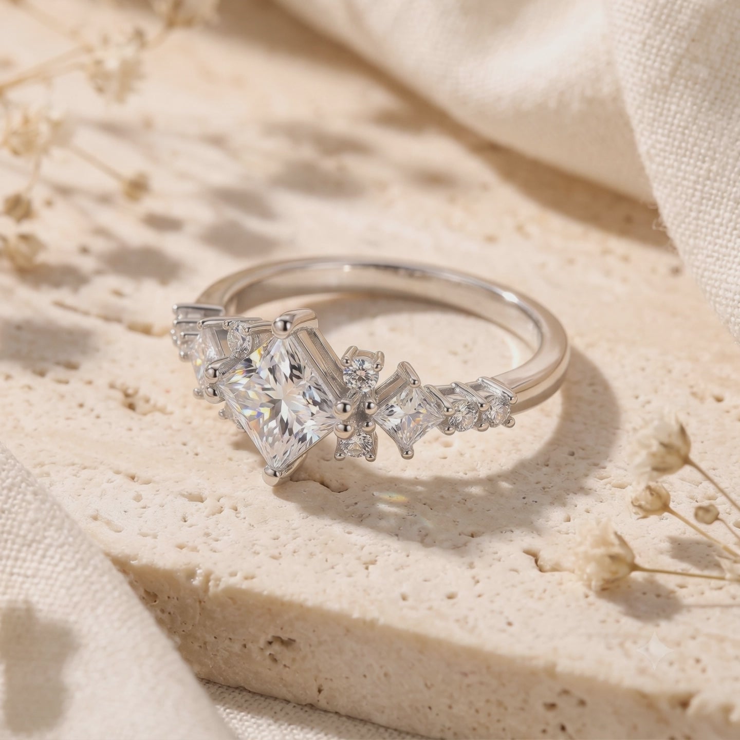 Silver ring with a kite-set princess-cut clear stone on a textured cream surface.