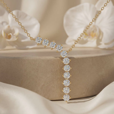 Close-up of a gold-tone moissanite Y-necklace displayed on a pedestal with white orchids.