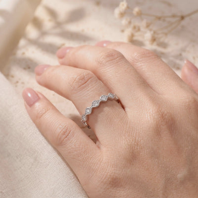 A silver wavy ring with round clear stones worn on a finger against a softly lit neutral background.