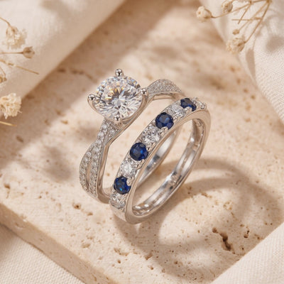Silver solitaire and alternating blue-and-clear stone bands displayed upright on a beige textured stone surface.