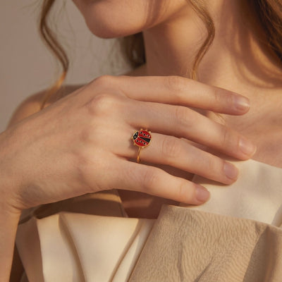 Gold-tone bypass ring with a red and black enamel ladybug, shown worn on a model's finger.