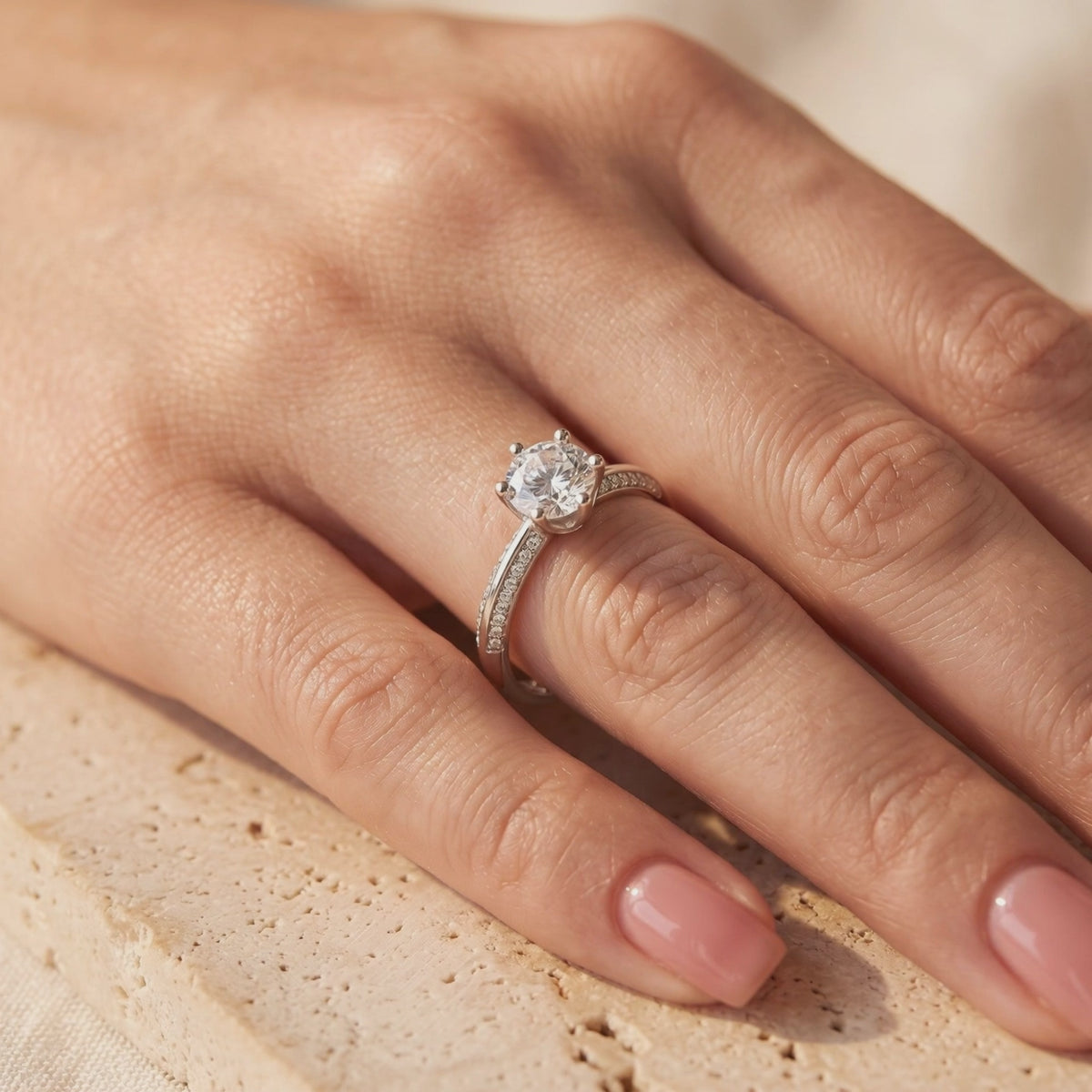 Silver solitaire ring with a round clear stone and pavé accents, worn on a hand.