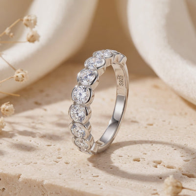 Upright silver ring with round clear stones, showing an S925 stamp inside, on a textured stone surface.