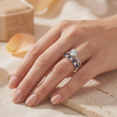 Hand wearing the silver ring set, with a round solitaire, pavé shoulders, and an alternating blue and clear stone band.