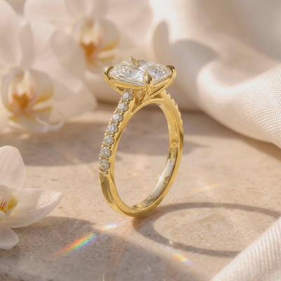 Side view of a yellow-gold-tone pavé ring with a radiant-cut center stone displayed among white orchids