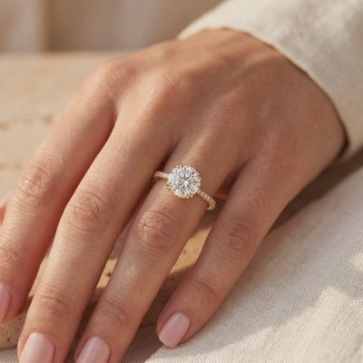 Round moissanite ring with pavé shoulders worn on a finger in warm light.