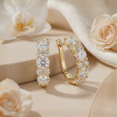 Pair of gold-tone hoop earrings with alternating round moissanites on a beige surface beside white flowers.