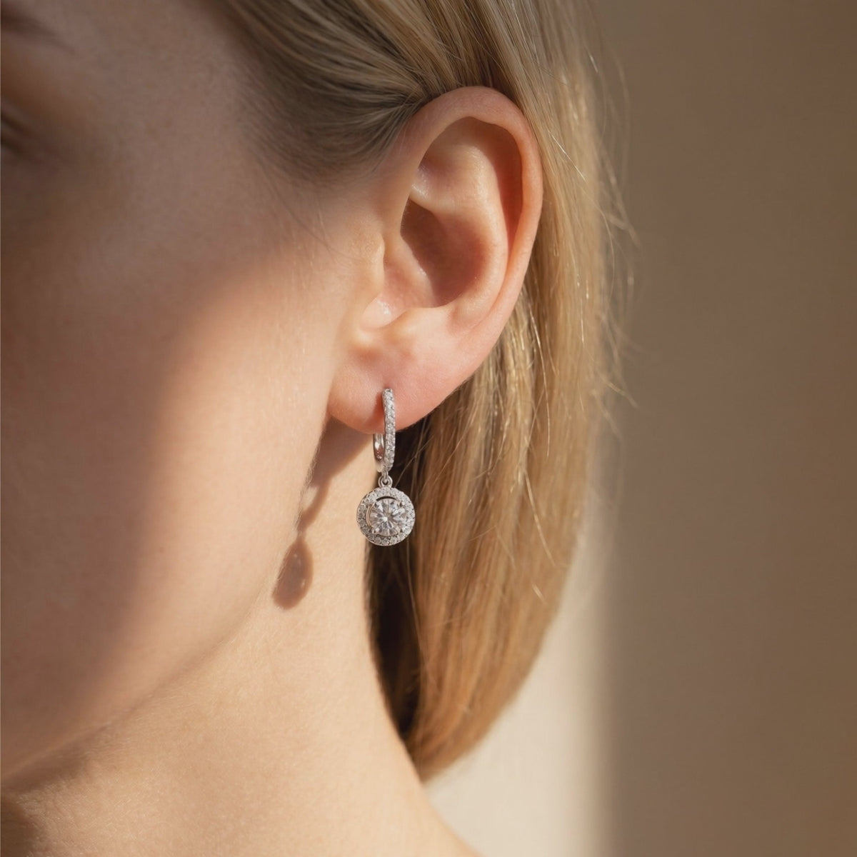 Silver-toned round moissanite halo drop earring worn on a woman's earlobe.