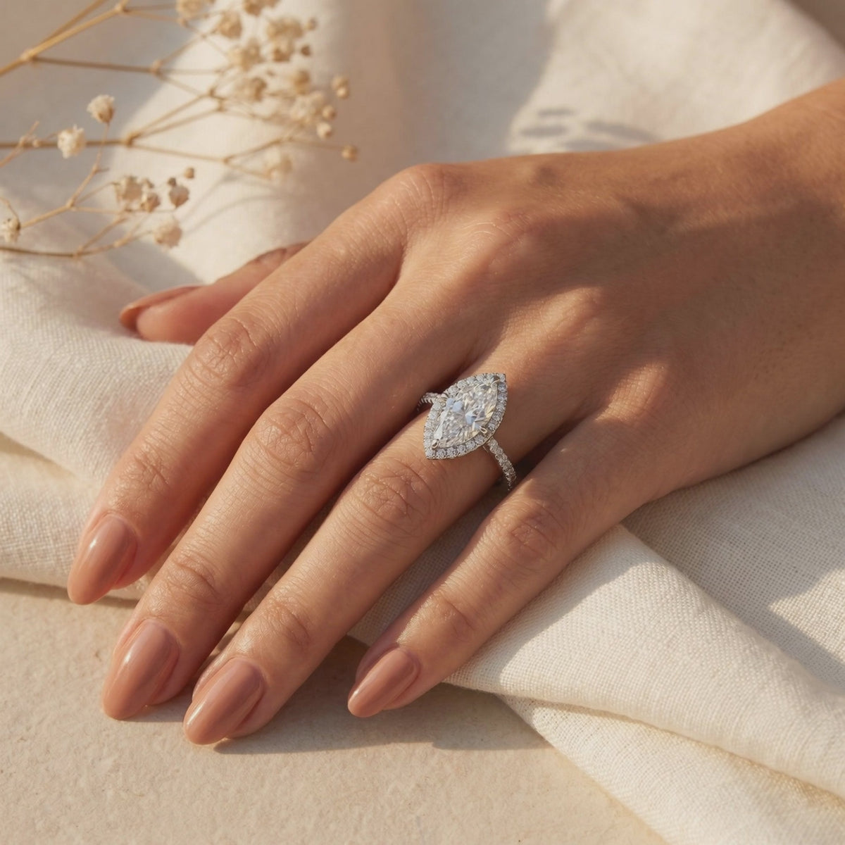 Silver marquise moissanite halo ring with a pavé band worn on a hand.
