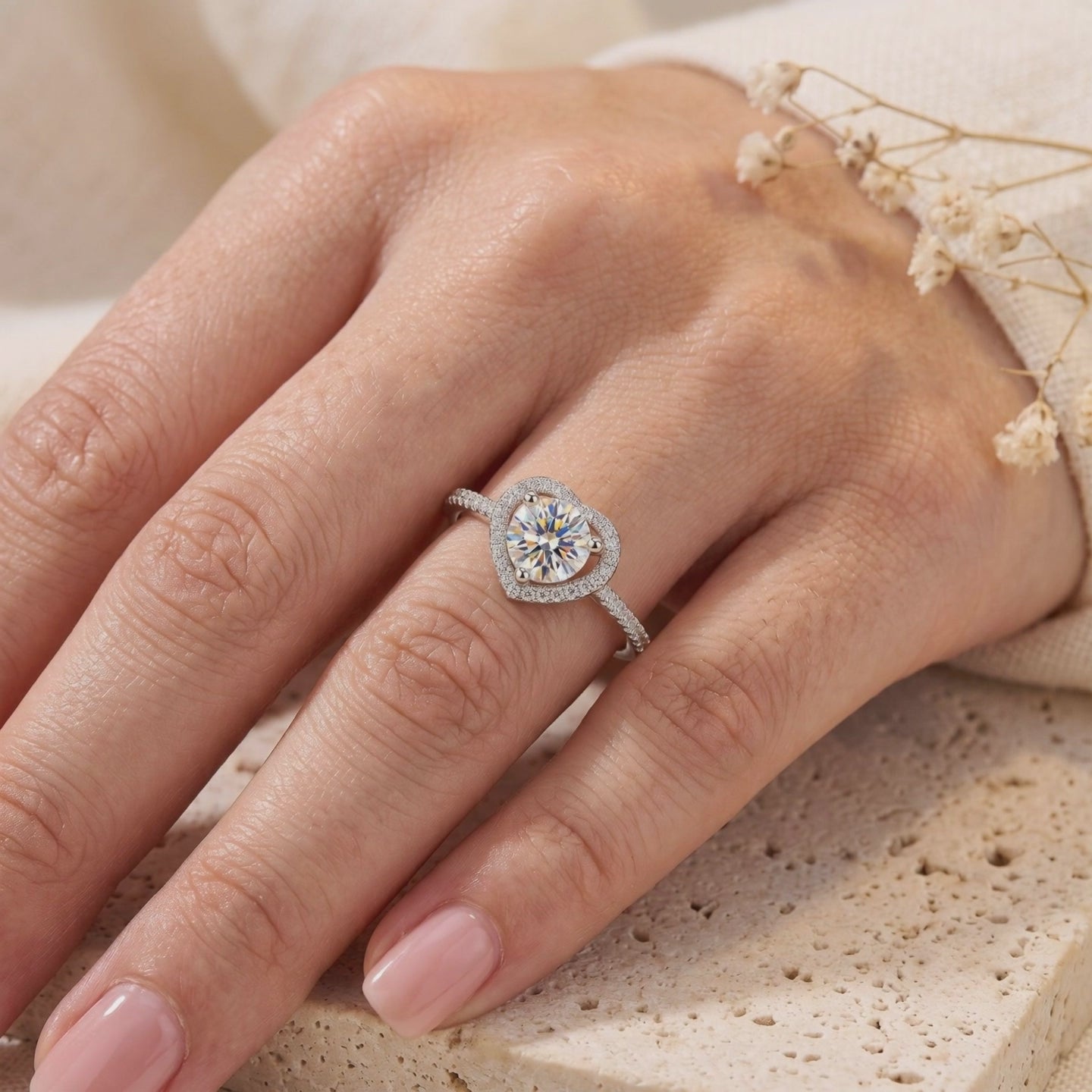 Hand wearing a silver ring with a round center stone surrounded by a heart-shaped stone halo.