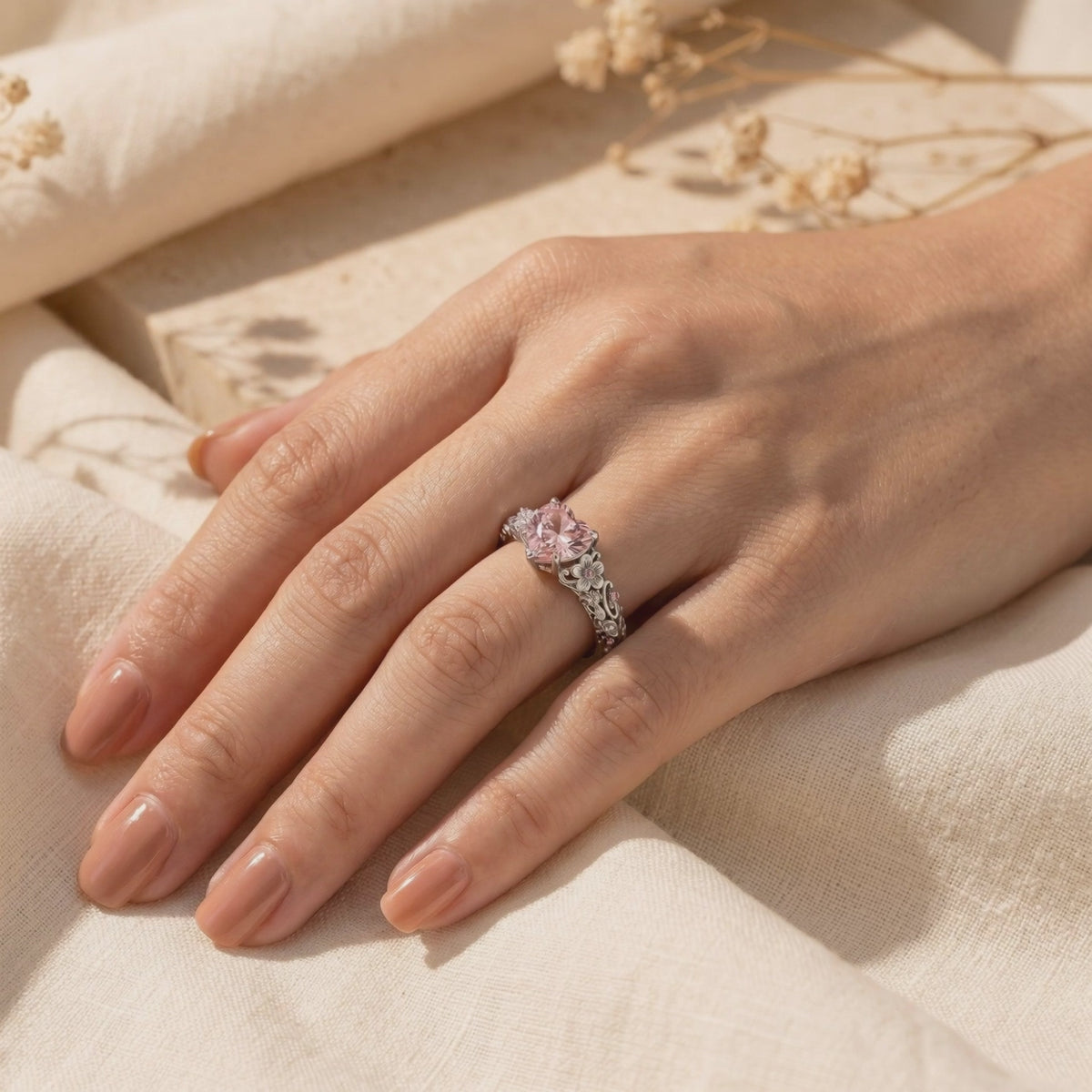 Silver ring with a heart-shaped pink centerpiece and floral band detailing worn on a hand.