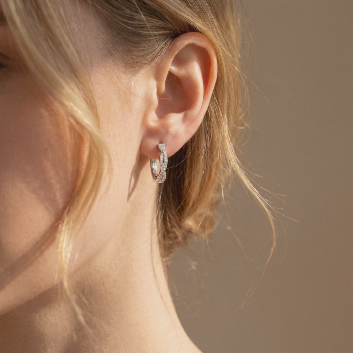 Single twisted silver hoop earring with round moissanite accents worn on a woman's ear
